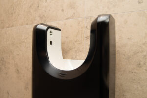 Primo piano di un moderno asciugamani touchless bianco e nero, montato su una parete piastrellata beige in un bagno.