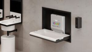 Un moderno bagno pubblico con un fasciatoio bianco ripiegabile per l'uso, accanto a un dispenser di carta mani e un lavandino bianco con sanitari neri.