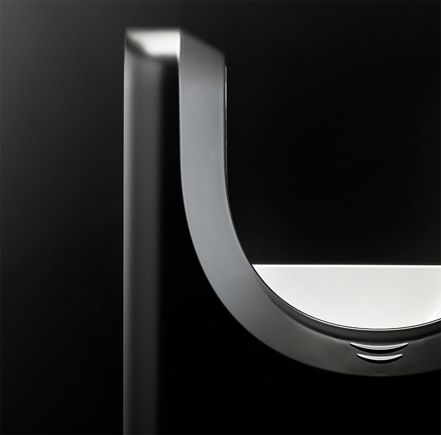 Primo piano di un oggetto moderno e minimalista in nero e argento con un design curvo a forma di U su uno sfondo scuro, caratterizzato da una superficie riflettente e bordi lisci.