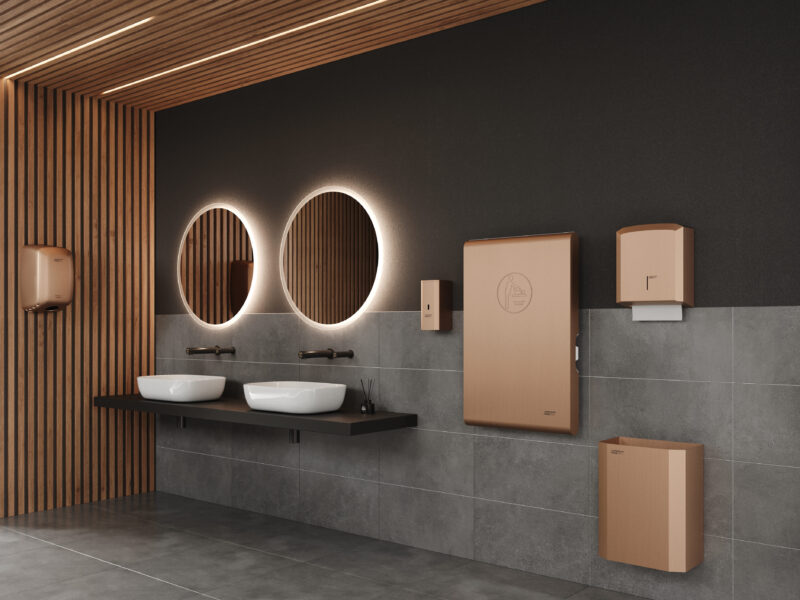 Moderna toilette pubblica dal design elegante, con due specchi rotondi retroilluminati, lavandini a vaschetta e apparecchi a parete di colore marrone su pareti piastrellate grigie e pannelli in legno.